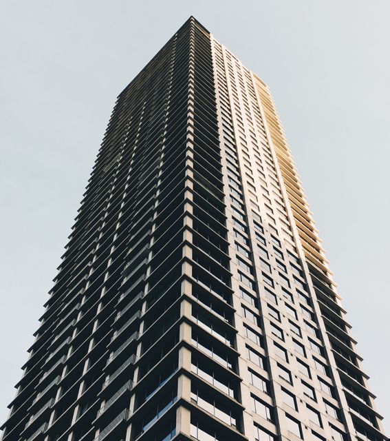 This image shows a striking low angle view of a tall office building against the sky, making it perfect for use in business, real estate, and architecture-related projects. It can be used in promotional materials, website backgrounds, or social media posts highlighting urban life, modern architecture, or corporate settings.