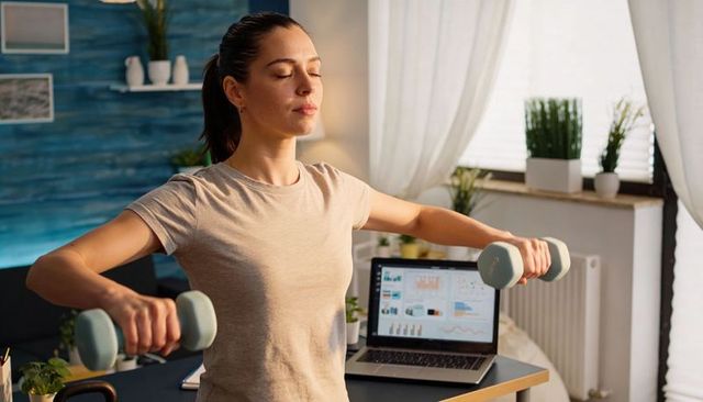 Remote work fitness: woman doing lateral raises with pastel dumbbells beside laptop