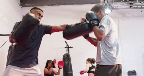 Coach guiding boxer hitting focus mitts during high-intensity gym pad drills