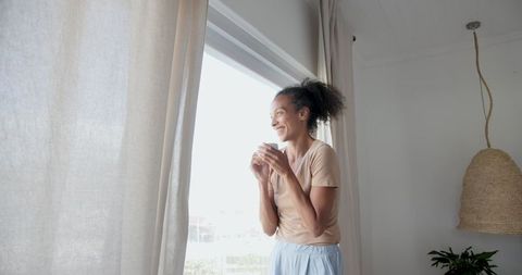 Smiling Woman Sipping Coffee by Window in Bright Minimalist Room