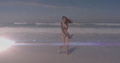 Joyful woman in floral bikini enjoying deserted beach with ocean waves