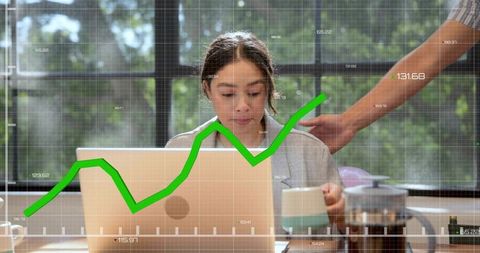 Professional woman working on laptop holding mug with rising green analytics graph overlay