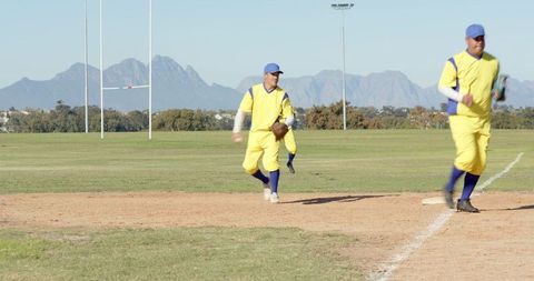 Baseball Players Running and Fielding in Yellow Uniforms on Sunlit Grass Field