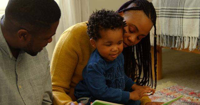 Front view of young black parents and son reading a story book and sitting on floor at home. Son sitting on mothers lap and father looking at him 4k
