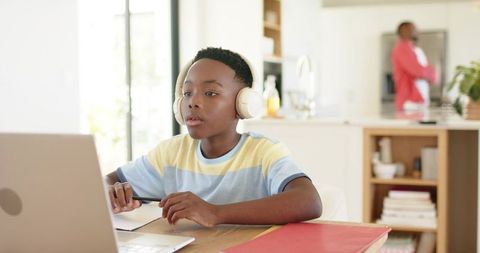 African american boy wearing headphones studying online at home kitchen table