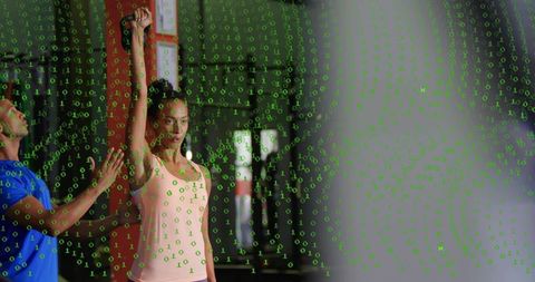 Woman lifting dumbbell overhead while coach spots with green binary code overlay