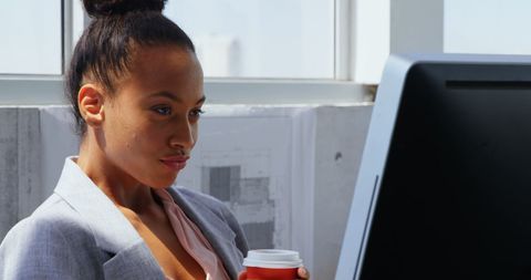 Focused African American Businesswoman Checks Computer While Holding Coffee Cup
