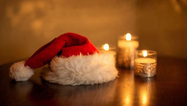 Santa Hat Lying on Wooden Table with Candlelight, Radiating Cozy Christmas Warmth