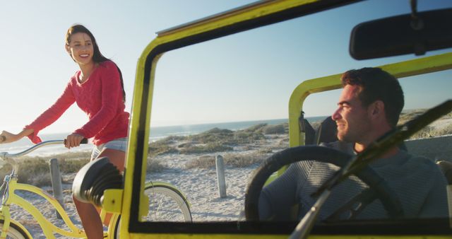 Happy caucasian woman riding a bike next to man in beach buggy by the sea. beach stop off on summer holiday road trip.