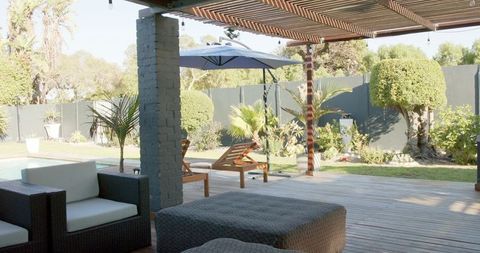 Sunlit backyard deck with slatted pergola, rattan lounge seating and poolside sunloungers