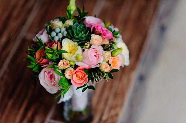 Colorful bridal bouquet featuring roses and succulents arranged with greenery against a wooden background. Ideal for wedding decor inspiration, bridal magazines, event planning guides, and floral arrangement ideas.