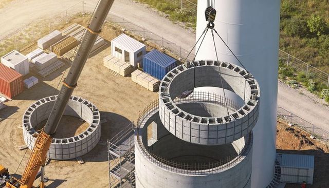Crane lowering precast concrete ring onto wind turbine tower at construction site