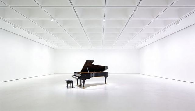 Black grand piano centered in minimal white gallery with raised lid and bench on casters