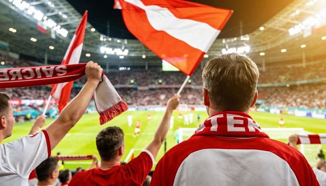 Red and white fans cheering and waving flags in packed stadium under floodlights at night