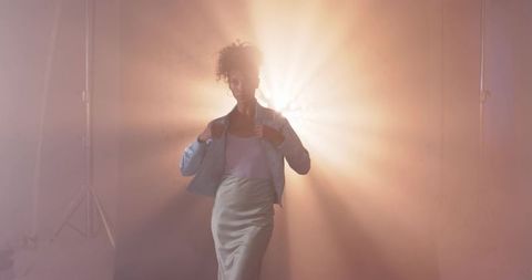 Backlit african american woman posing and adjusting jacket with dramatic light beams