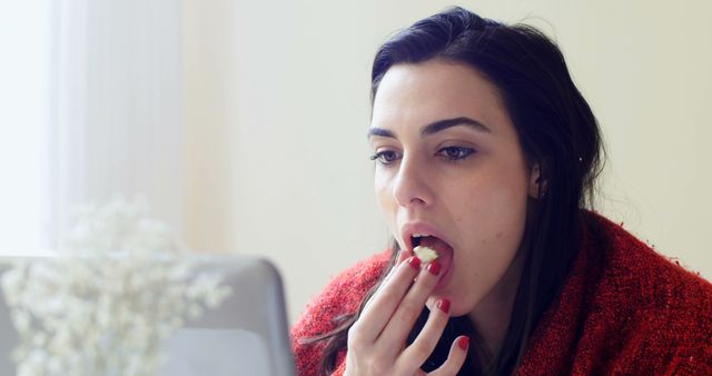 A young Caucasian woman is eating while focused on her laptop screen, with copy space. Her multitasking reflects the common practice of combining mealtime with work or leisure screen time.