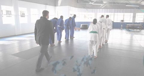 Instructor in suit walking toward bowing martial artists in dojo training and discipline