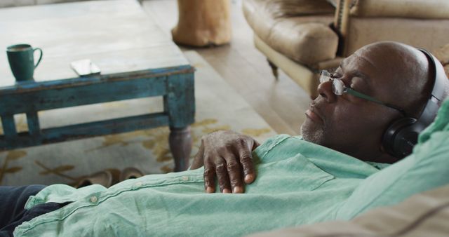 Elderly man relaxing on a couch wearing headphones, suggesting a moment of tranquility and peacefulness. Could be used to illustrate concepts of relaxation, senior lifestyle, or leisure activities. Suitable for websites and articles focusing on retirement, mental health, leisure, and senior care.
