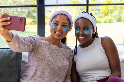 Asian and african american friends taking selfie during skincare night with eye patches