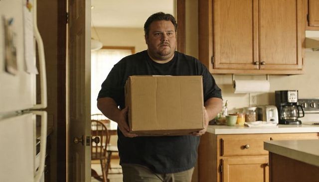 Mid-40s Man Carrying Cardboard Box Into Home Kitchen Walking Through Sunlit Doorway