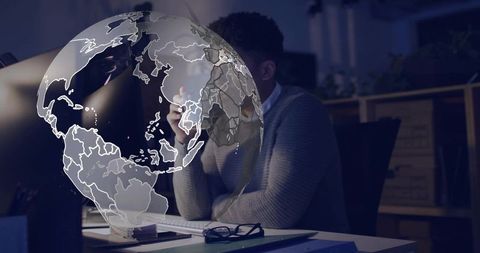 Professional working late analyzing data with holographic globe overlay at desk