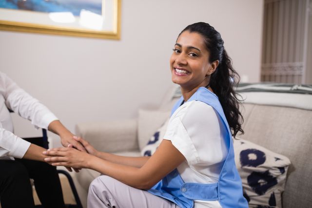This image depicts a smiling female doctor holding a patient's hands during a home visit, showcasing compassion and trust in patient care. Ideal for use in healthcare promotions, medical service advertisements, and articles about home healthcare and patient support.