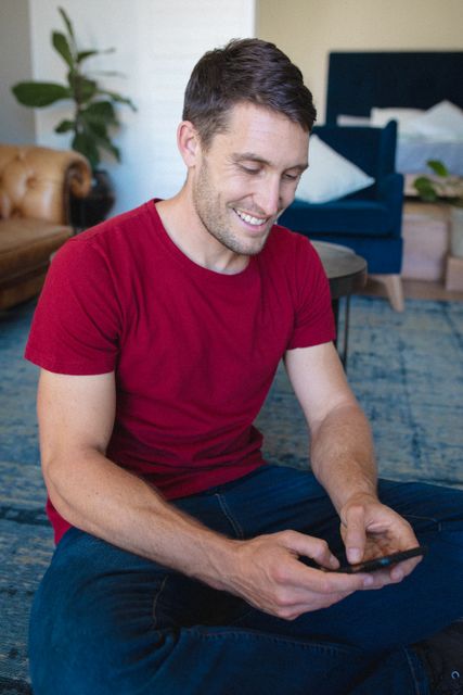 Caucasian man smiling while using smartphone sitting in the living room at home - Download Free Stock Photos Pikwizard.com