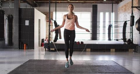 Athletic woman jumping rope in loft boxing gym for cardio training and hiit