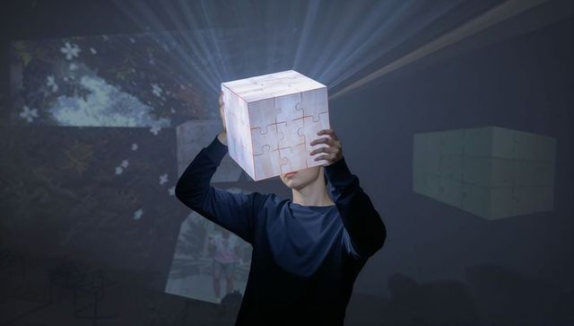 Holding glowing puzzle cube projecting light beams in immersive gallery installation