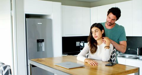 Couple Relaxing in Modern Kitchen Discussing near Laptop