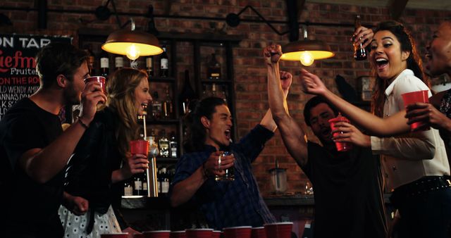 Group of friends in a bar celebrating and playing beer pong. They are cheering and enjoying drinks, portraying excitement and friendship. Perfect for advertisements related to nightlife, partying, bars, social events, or youth culture promotions.