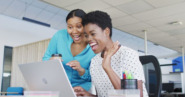 Two women in an office celebrating success while looking at a laptop. Ideal for content related to corporate achievement, teamwork, workplace environment, technology in business, and professional collaboration.