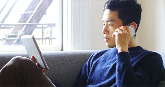 Young Asian Man Talking on Smartphone While Using Tablet - Download Free Stock Images Pikwizard.com