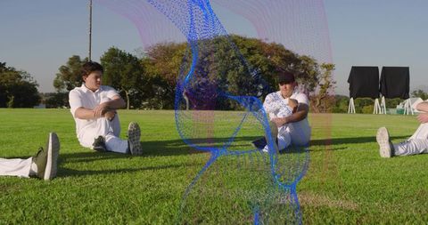 Cricket players stretching and sitting on outfield during team training on sunny oval