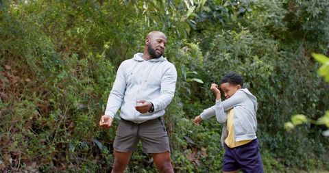 African american father and son practicing playful sparring on leafy forest trail walk