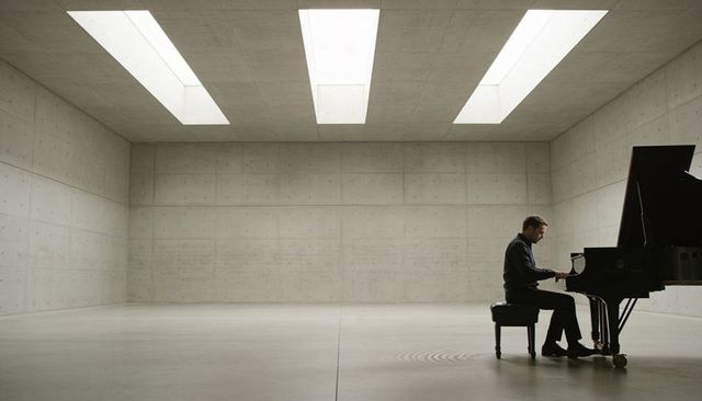 Pianist playing black grand piano in minimalist concrete hall with skylights