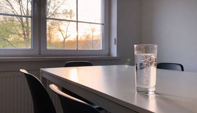 Minimal glass of sparkling water catching soft warm sunset light on white table by window