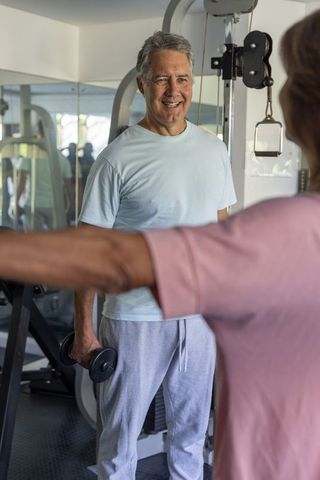 Senior couple exercising in gym smiling during strength training with dumbbells