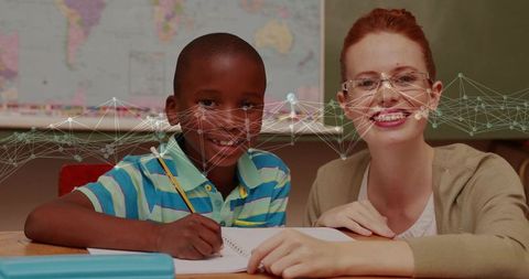 Smiling teacher guiding student writing at classroom desk, one-on-one tutoring moment