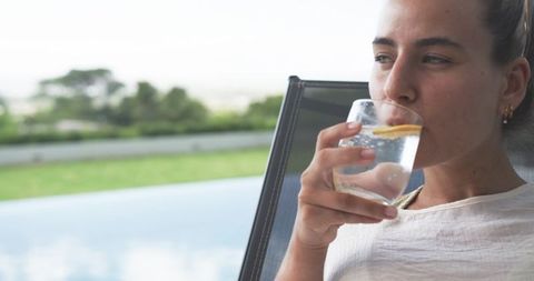 African american woman relaxing poolside sipping lemon water on modern patio with view