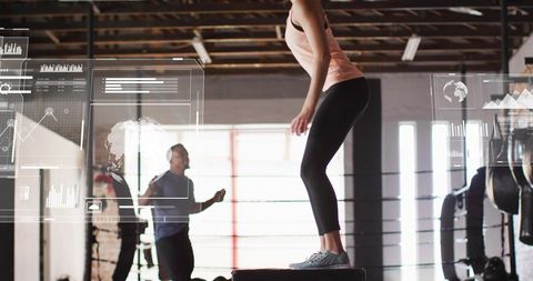 Woman performing plyo box jumps in industrial gym during partner hiit and jump rope training