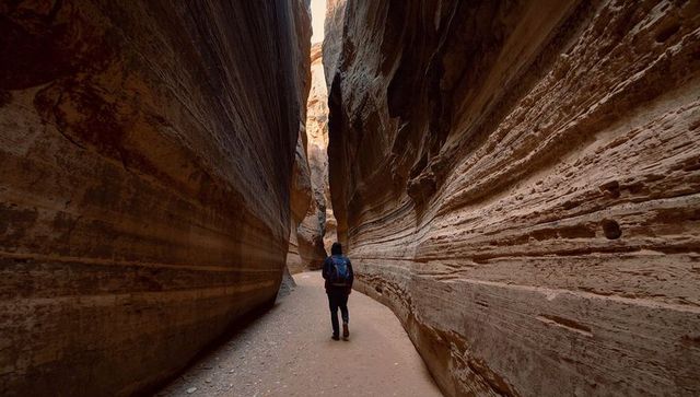 Solo hiker walking through narrow sandstone slot canyon with backpack and hiking boots