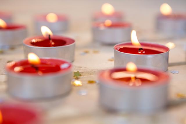 Red tealight candles burning with warm light, surrounded by star-shaped confetti. Ideal for use in holiday-themed designs, Christmas cards, festive decorations, romantic settings, and relaxation or spa-related content.