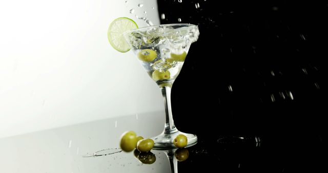 Close-up of a cocktail glass filled with a splashing martini, garnished with a slice of lime and accompanied by olives. The background features a striking contrast of black and white halves, enhancing the sophistication of the scene. Ideal for advertising bars, cocktail recipes, nightlife events, and party invitations.