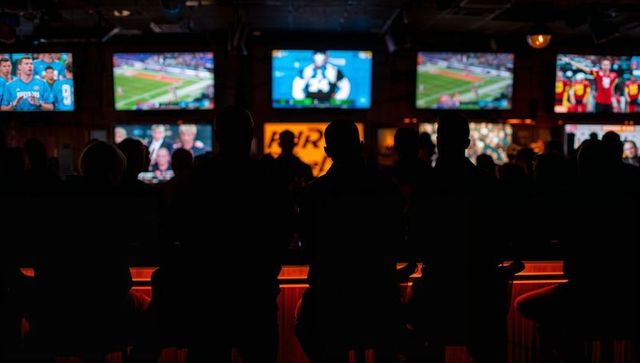 Backlit silhouettes watching multiple screens in sports bar with amber underglow