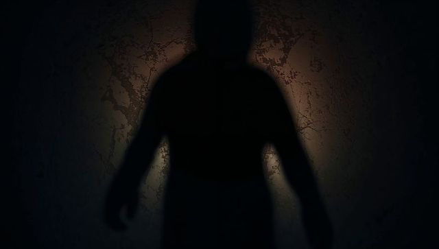 Silhouette figure casting oversized shadow on cracked plaster wall with warm halo backlight