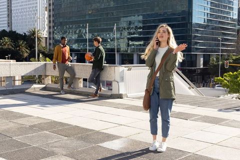 Young woman talking on phone on urban rooftop terrace while friends playing basketball