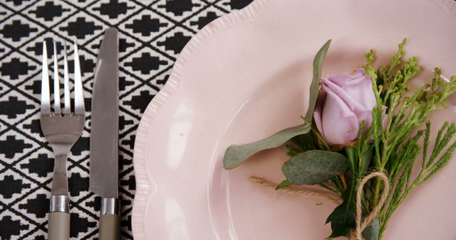 A detail view of an elegant table setting with a pink plate adorned with lavender flower and small greenery bouquet. Designed to create a charming dining experience, perfect for weddings, romantic dinners, or special occasions. Ideal for use in culinary blogs, dining etiquette websites, and event planning promotional material.