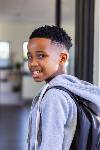 Confident african american schoolboy turning back wearing backpack and gray hoodie