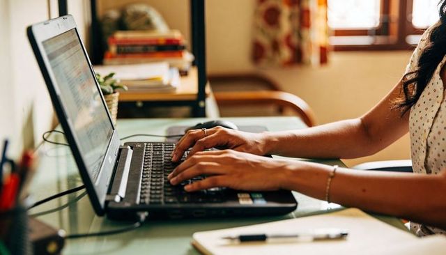 Woman typing on laptop at home workspace with notepad and plant, remote work lifestyle